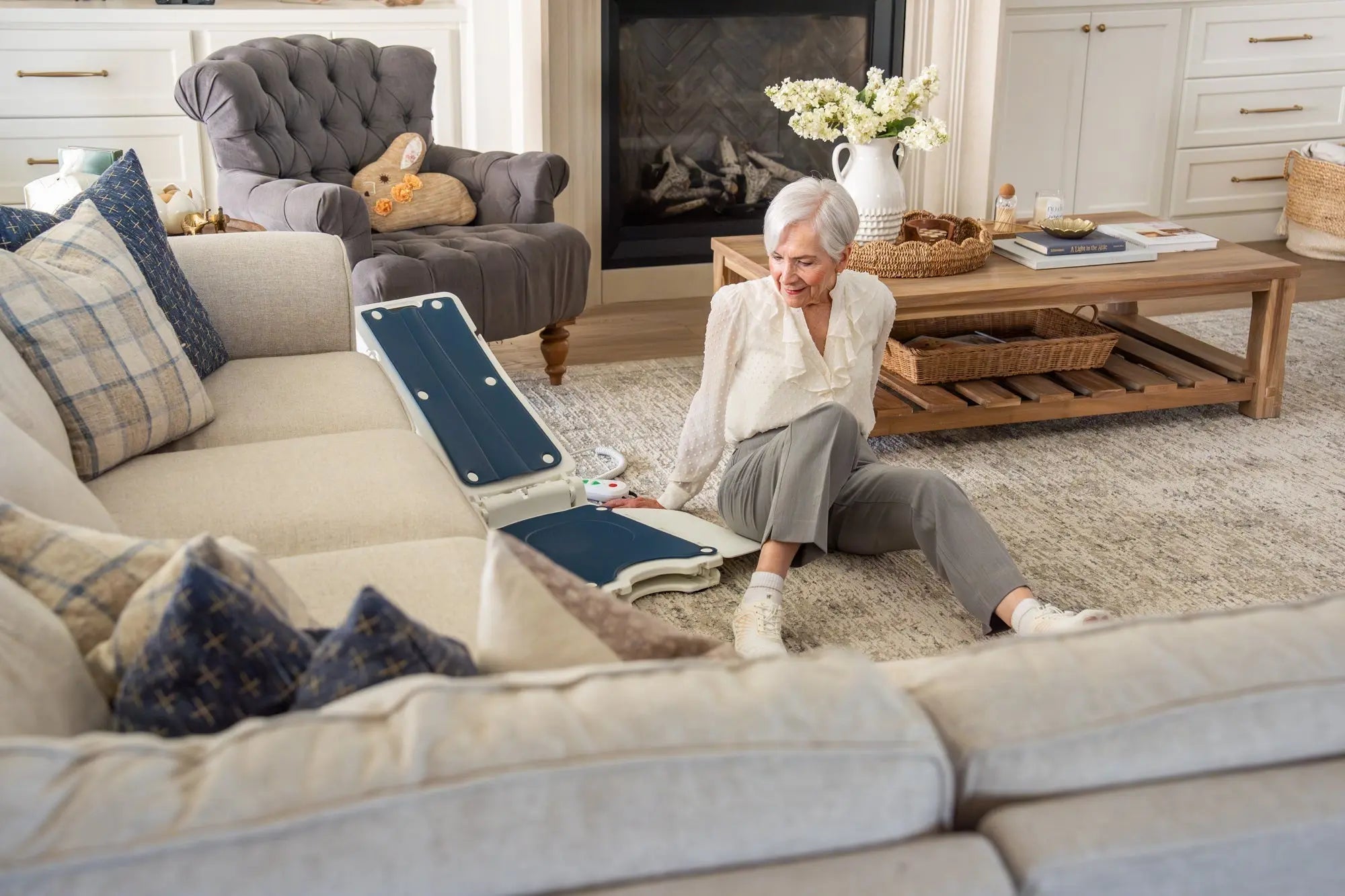 Older woman seated beside a portable electric floor lift chair in her living room.