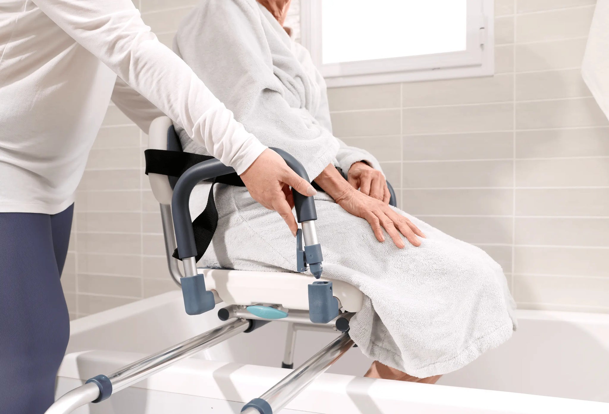 Caregiver assisting a senior seated on a sliding tub transfer bench.