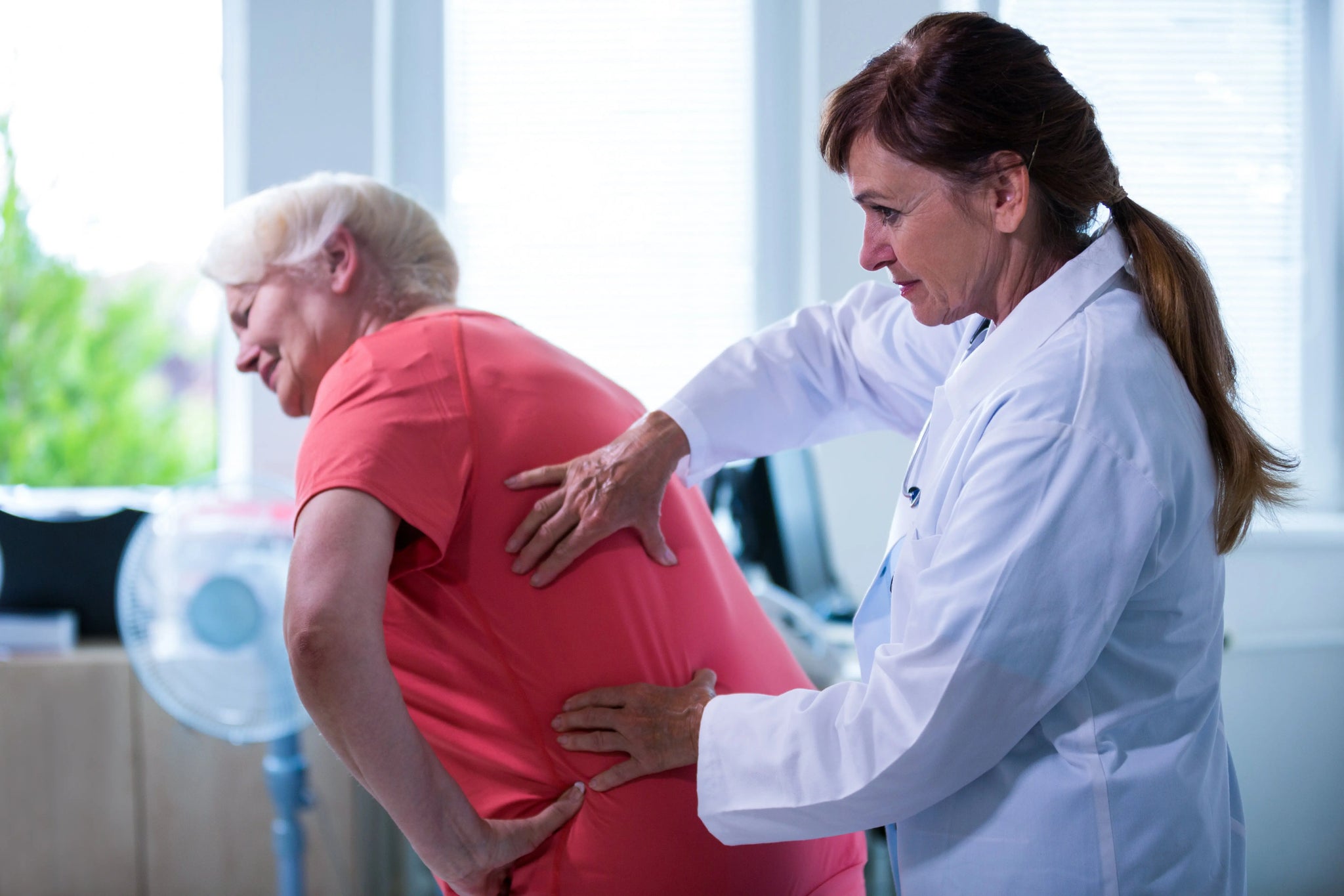 Doctor examining an older woman experiencing lower back pain from lumbago with sciatica.