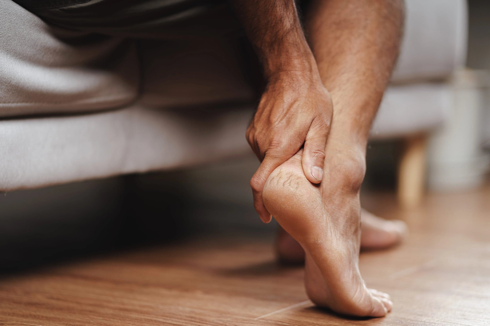 Man holding his heel while seated, illustrating foot discomfort linked to peripheral neuropathy.