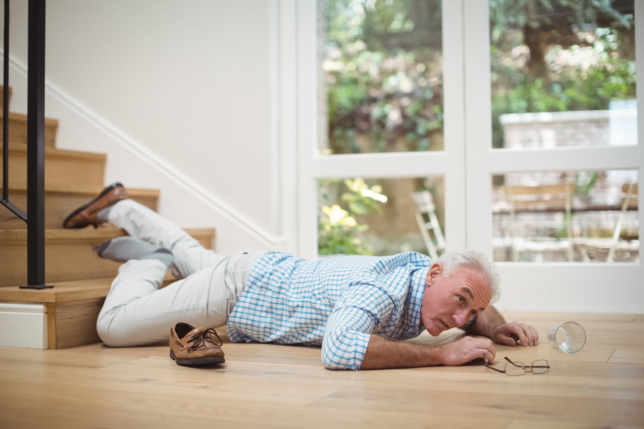 Older man lying on the floor after falling near a staircase at home, illustrating the risk of slips and falls in older adults.