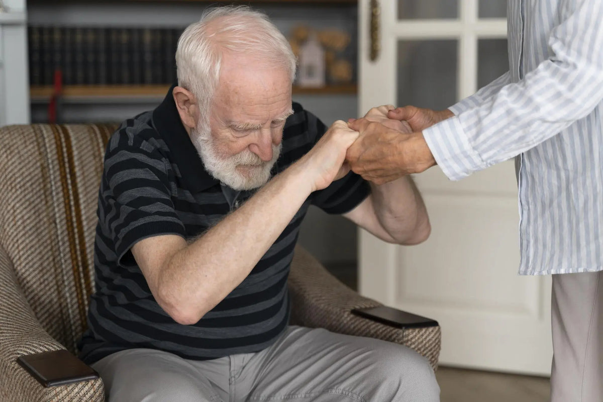 Caregiver helping a senior man stand safely from a chair during stroke recovery at home.