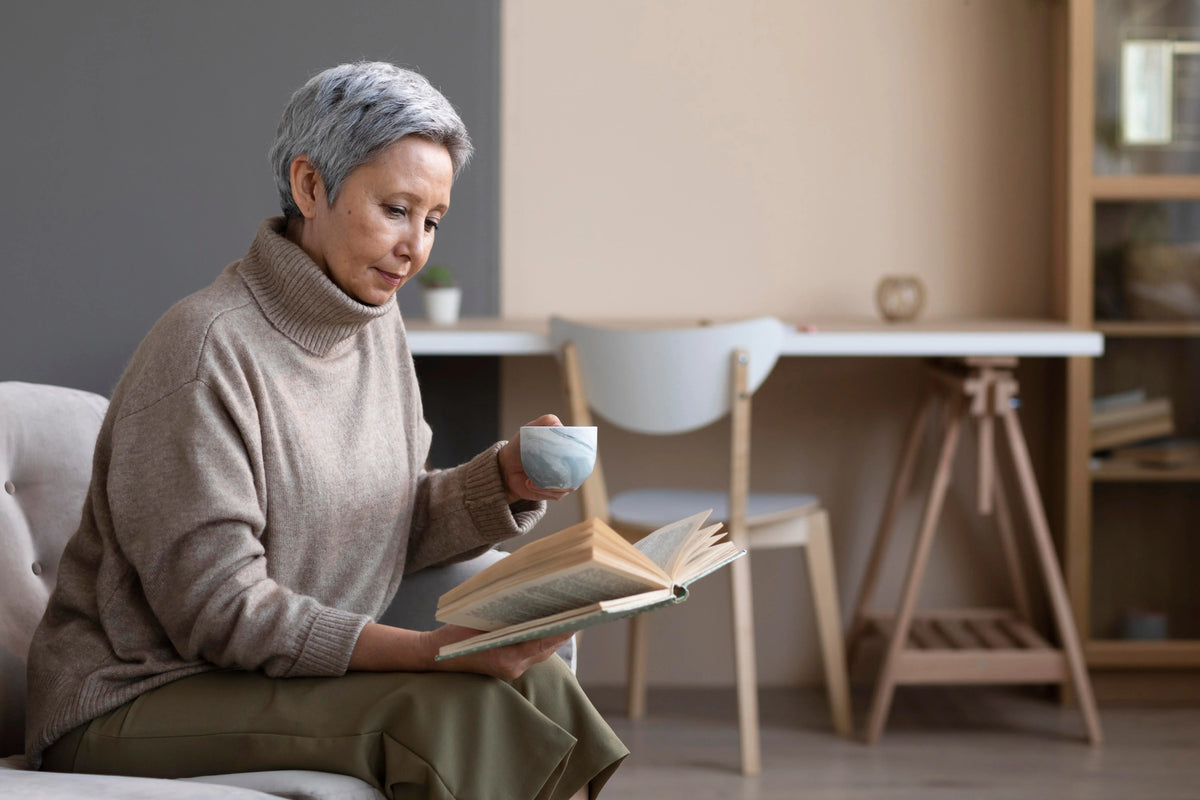 Senior woman enjoying a book and a cup of tea while relaxing in a comfortable living room.