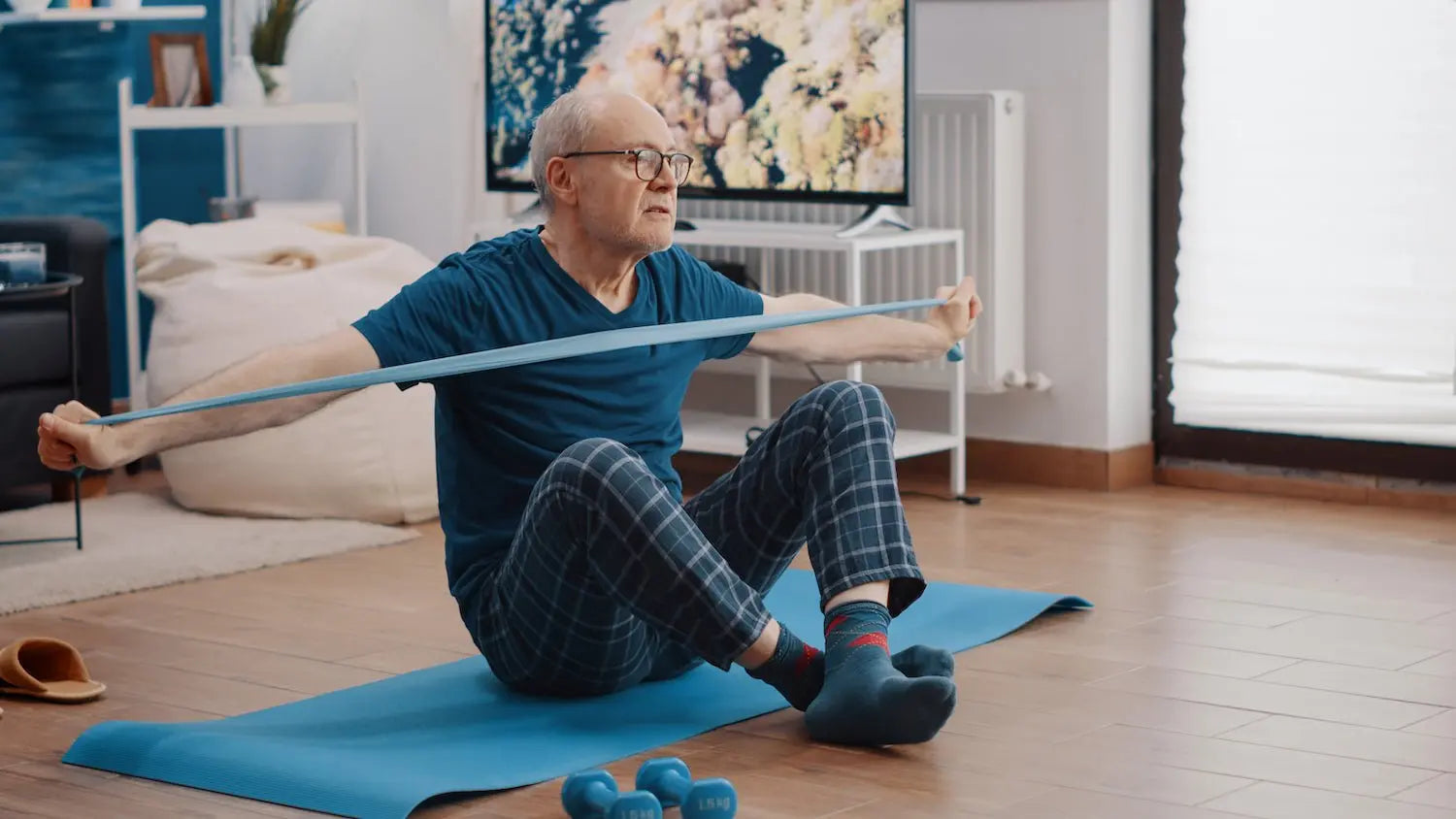 Senior performing seated resistance band exercises on a mat at home with dumbbells nearby.